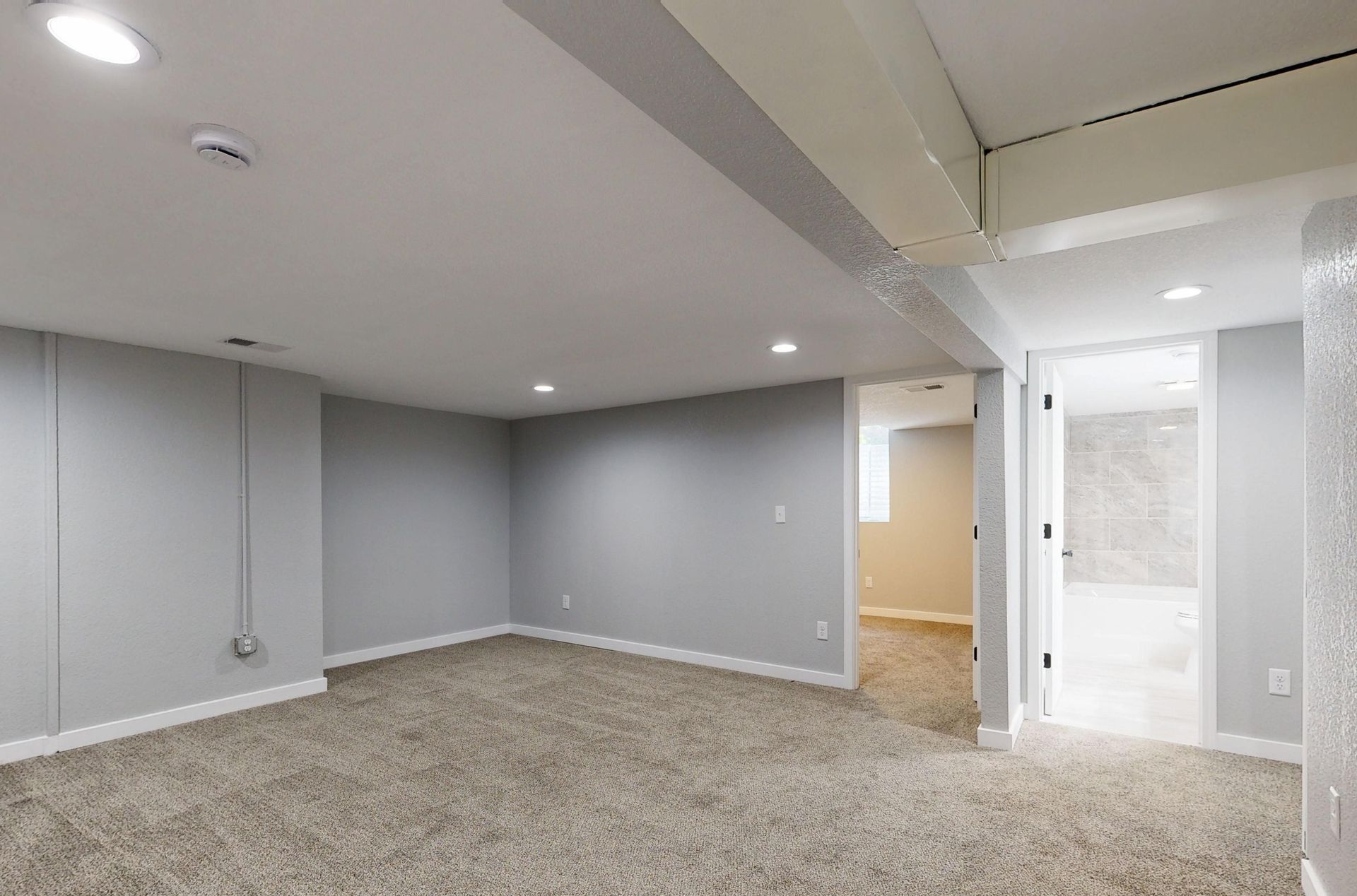 Empty basement room with neutral carpet and recessed lighting.