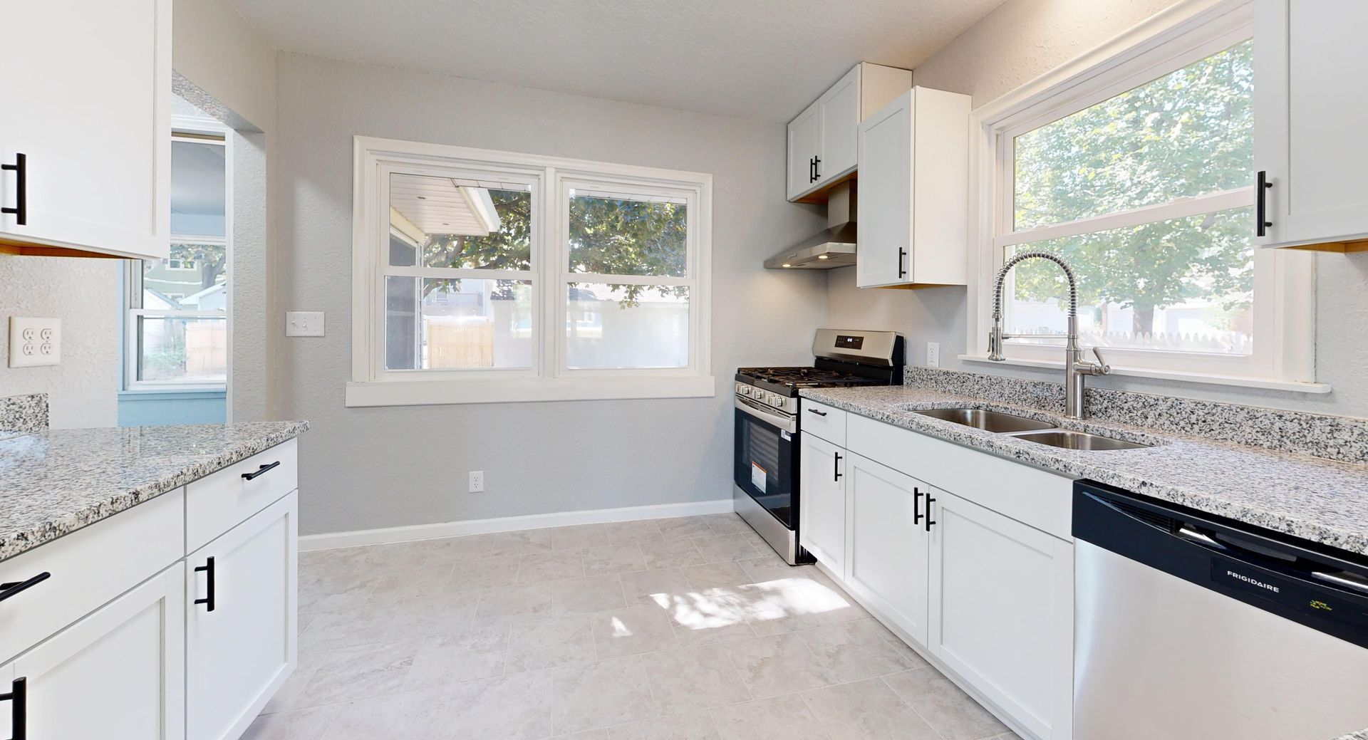 Sunlit modern kitchen featuring granite countertops and sleek white cabinetry.